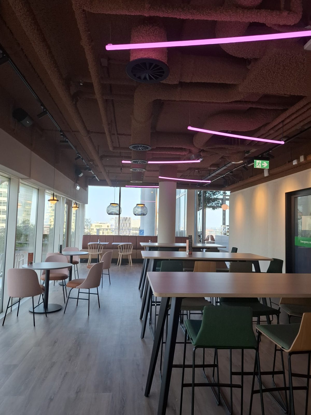 Dining floor with timber tables and the exposed acoustic ceiling, looking out over the Zuidas